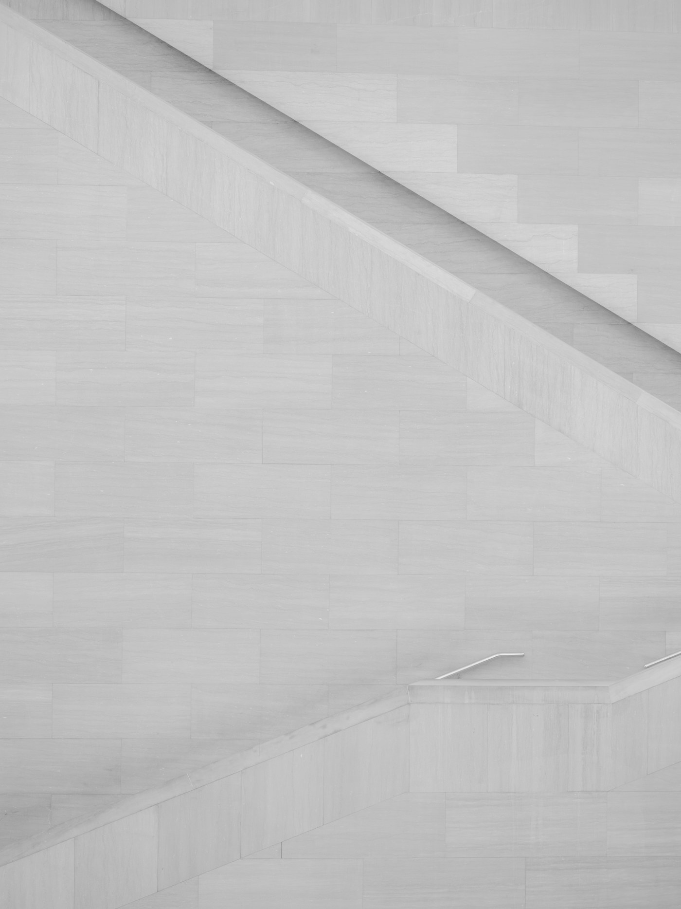 Minimalistinė šviesaus akmens laiptų geometrija su įstrižomis linijomis